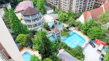A residential area with a swimming pool surrounded by trees and a multi-story building with balconies.