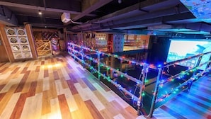 A room with a wooden parquet floor, a long table with string lights, and a television screen. - Diyicun Hot Spring Hotel (Dayi)