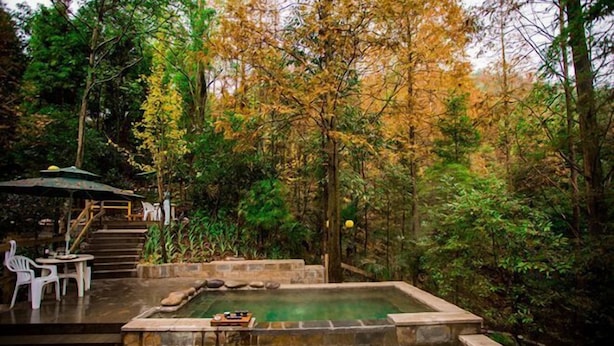 A hot spring surrounded by trees, with a small table and chairs nearby. - Diyicun Hot Spring Hotel (Dayi)