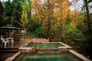 A hot spring surrounded by trees, with a small table and chairs nearby.