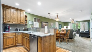 Una cocina con armarios de madera, lavavajillas y comedor con mesa y sillas.