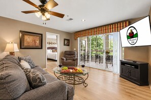A living room with a sofa, armchair, and coffee table with fruit. There is a television and a ceiling fan. - Big on Space, Big on Location • 4 King Suites Near Branson Shows (Branson)