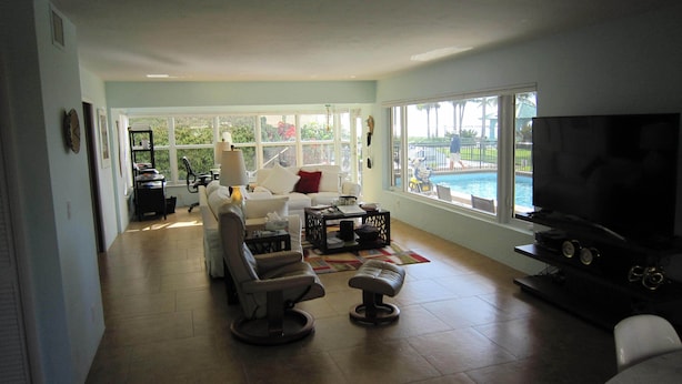 A spacious living room with a large TV, comfortable seating, a coffee table, and a view of a swimming pool. - Waterfront, Ground-Floor private residence with Ocean & Inlet views (Palm Beach Shores)