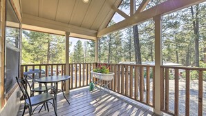 Une terrasse en bois avec une table et des chaises, un jardinier avec des fleurs et une vue sur une forêt.