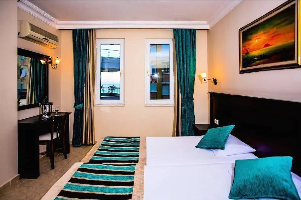 Une chambre d’hôtel avec un lit, un bureau, une chaise, une fenêtre avec des rideaux et un tableau au mur.