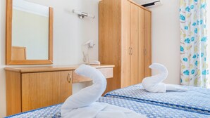 Habitación de hotel con armario de madera, espejo, lavamanos y dos camas con ropa de cama a cuadros azules.