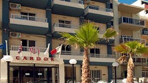 Un edificio de varios pisos con balcones, un cartel que dice "CARDOR" y palmeras en el frente.