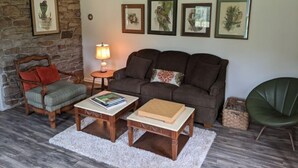 Una sala de estar acogedora con una pared de piedra, un sofá, dos mesas de centro de madera, una lámpara y cuadros en la pared.