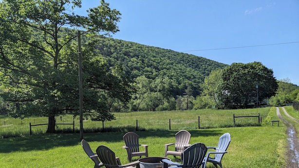 Un espacio al aire libre con césped y sillas Adirondack dispuestas alrededor de un brasero.