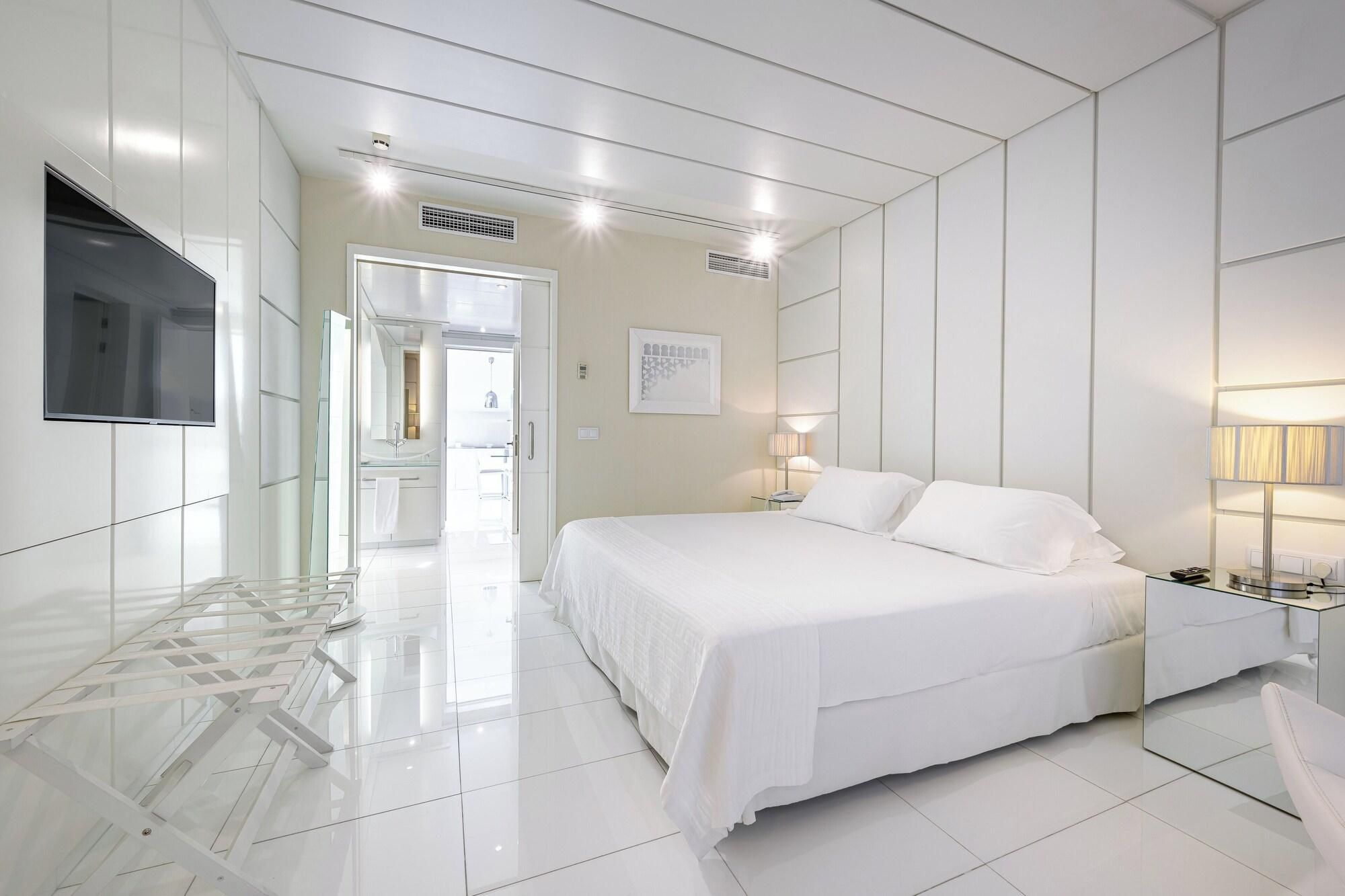 A modern hotel room with a large bed, a bedside table, a flat-screen TV, and a bathroom visible through an open door.