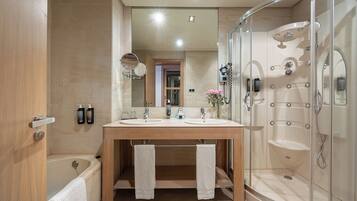 Un baño moderno con tocador doble lavamanos, ducha con cerramiento de vidrio y puerta visible que da a otra habitación.
