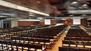 A conference room with rows of chairs and tables, a wooden floor, and a ceiling with recessed lighting. - Nelva (Murcia)