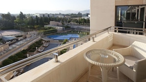 A balcony with wicker furniture, a glass table, and a view of a swimming pool and surrounding buildings. - Nelva (Murcia)