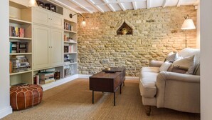 Un coin lecture chaleureux avec un mur en pierre, une bibliothèque, un pouf en cuir et un fauteuil confortable.
