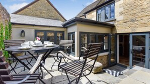 Une terrasse avec une table ronde, des chaises et un petit coin jardin.