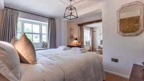 Une chambre avec un grand lit, une fenêtre avec des rideaux, un luminaire suspendu et un mur en pierre.