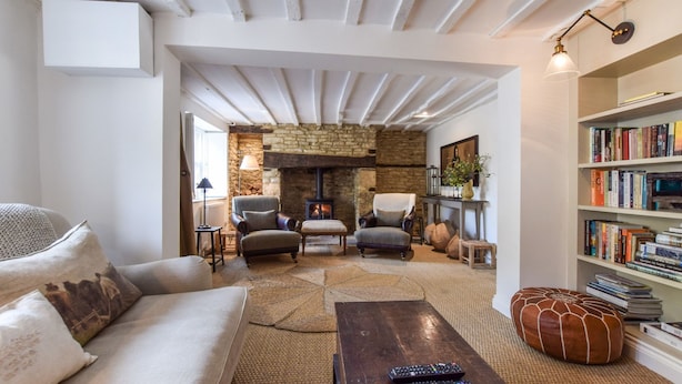 Un salon chaleureux avec une cheminée en pierre, deux fauteuils, un canapé et une bibliothèque remplie de livres.
