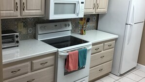 Une cuisine avec des meubles de couleur bois clair, un micro-ondes blanc, une cuisinière, un grille-pain et un réfrigérateur.