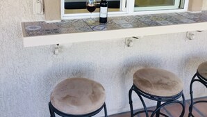 Une cuisine avec une fenêtre, une bouteille de vin et deux tabourets.