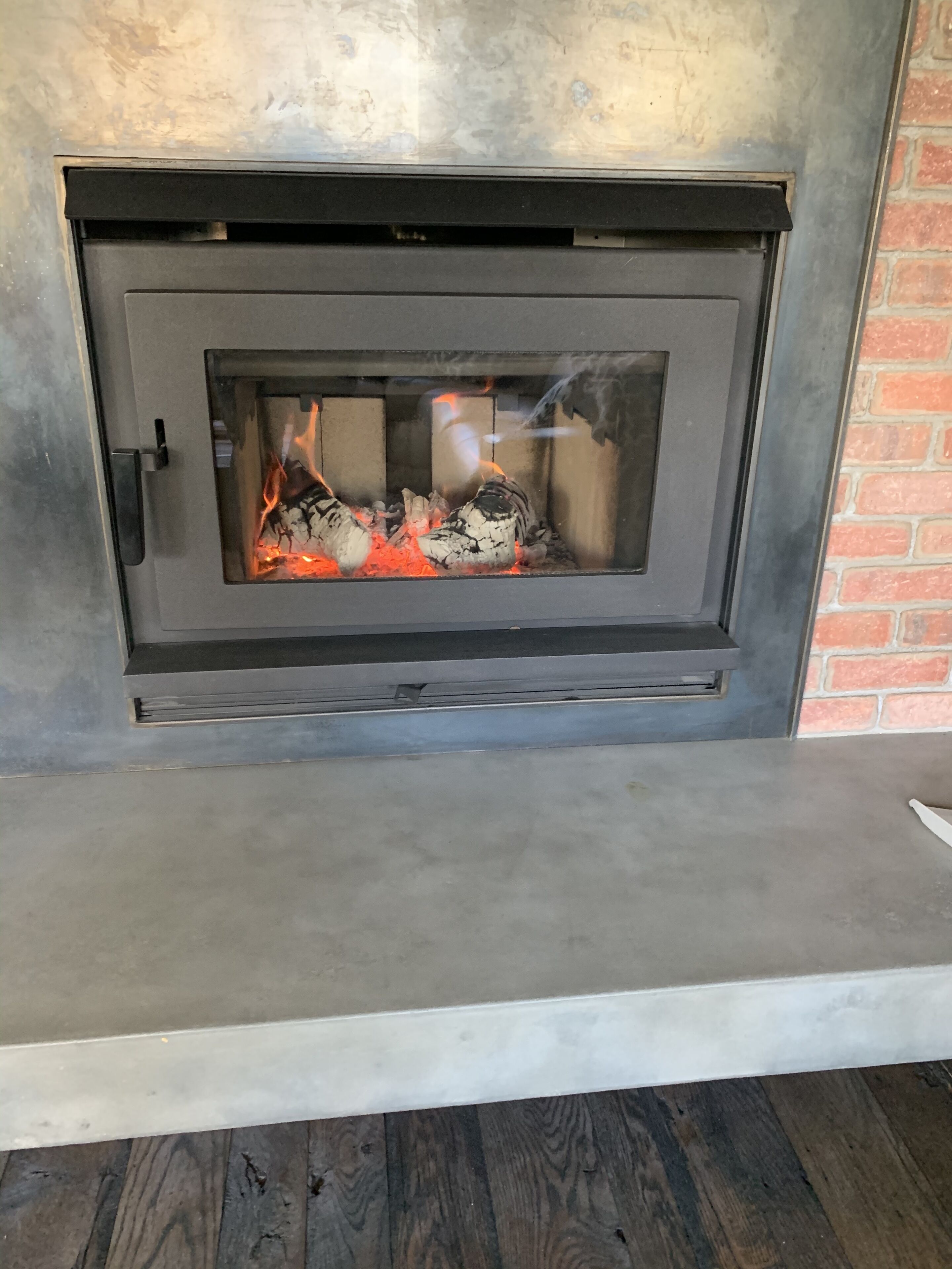 Ein moderner Kamin mit Glasfront, Metallrahmen und einer angrenzenden Ziegelwand.