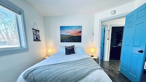 Ein Schlafzimmer mit einem Bett, zwei Nachttischlampen, einem Wandbild und einer Tür zu einem weiteren Raum.