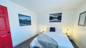 A bedroom with a bed, two bedside tables, a red door, and two wall-mounted pictures.