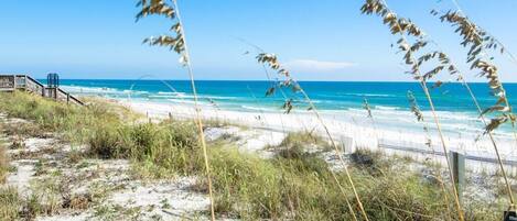 A beach with sand, grass, and a wooden boardwalk leading to the ocean.