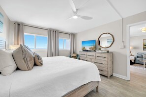 Un dormitorio con una cama grande, un ventilador de techo, un aparador, un espejo y vista al océano.