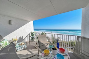 A balcony with a view of the ocean, a table with various items, and a chair. - 🌞Beach House 201A - Salt Water Retreat | Gulf Views + Seasonal Beach Service🌞 (Miramar Beach)