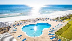 A pool with a unique heart-shaped design, surrounded by lounge chairs and a view of the beach.