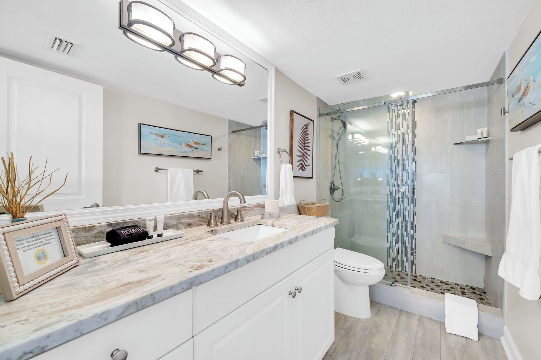 A modern bathroom with a glass shower enclosure, a large mirror, and a marble countertop.
