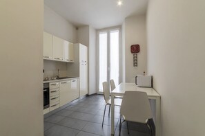 A modern kitchen with white cabinets, a dining table with chairs, and a clock on the wall.