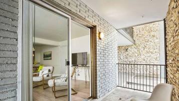 A modern interior with a glass door leading to a balcony, a seating area with a sofa and armchairs, and a stone wall.