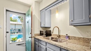 A kitchen with granite countertops, a stainless steel sink, a microwave, and a view of a swimming pool through a door. - Walk to Golf Course! Near Lake + Pool w Parking (Austin)