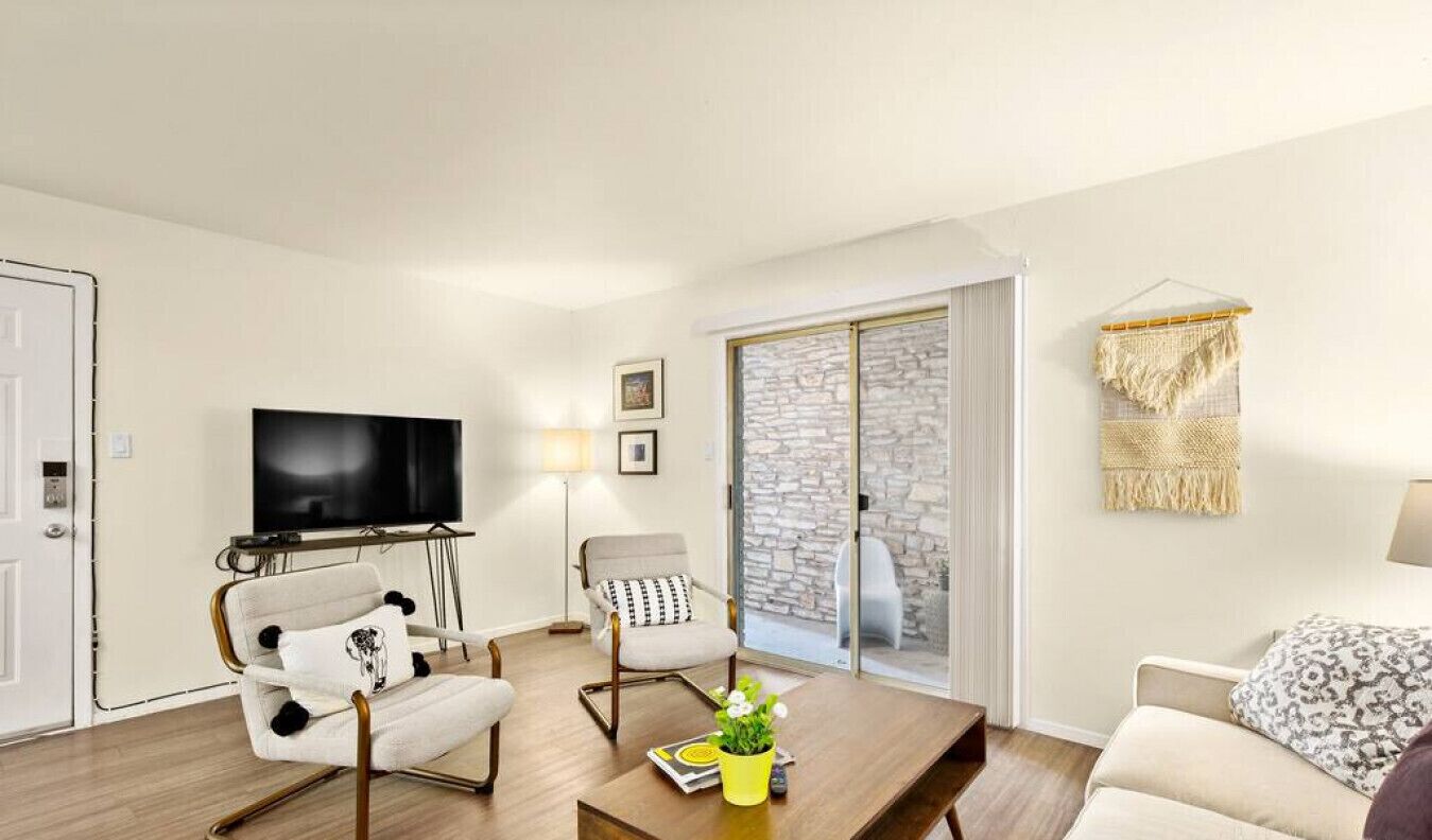 Een moderne woonkamer met een flatscreen televisie, een bank, een bijzettafeltje met een plant en een stenen muur.