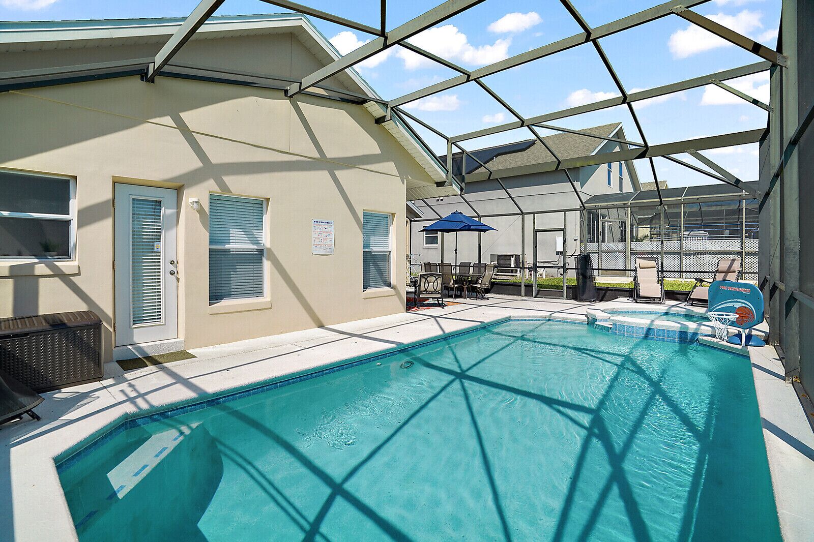 An indoor swimming pool with clear water, surrounded by a covered area with chairs and a basketball hoop.
