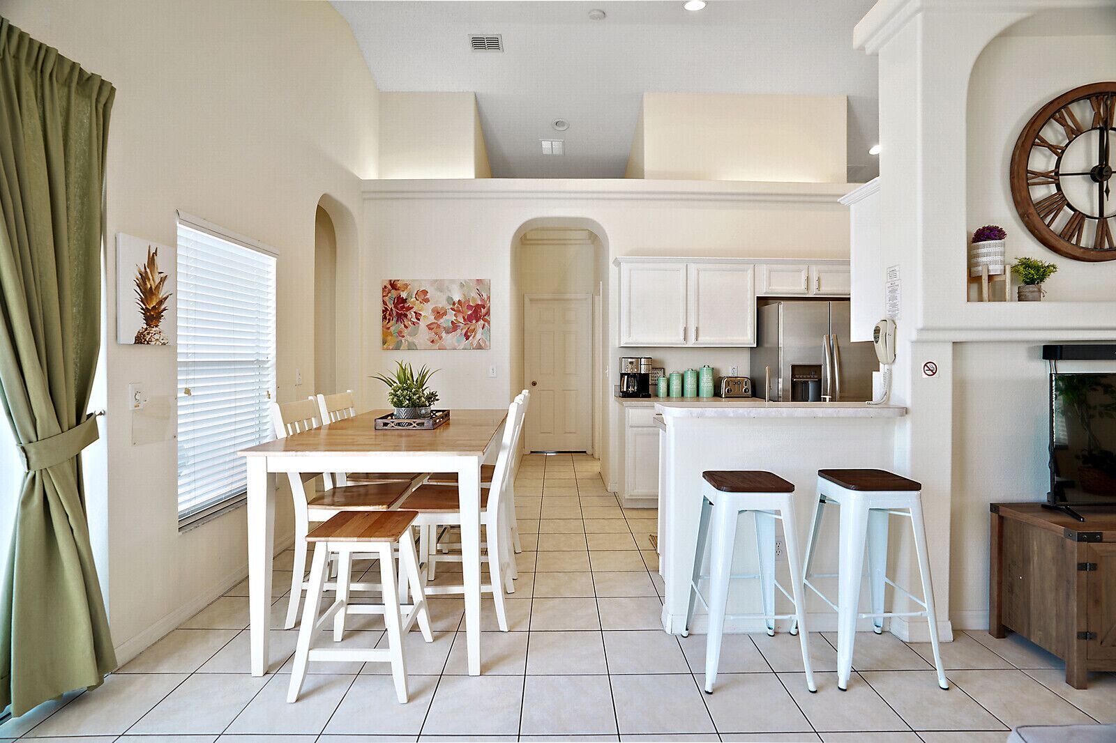 A modern kitchen with white cabinetry, a central island with stools, and a dining area with a wooden table and chairs.