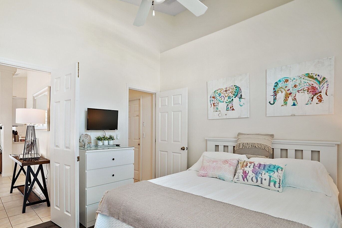 Un dormitorio con cama, cómoda, televisor y dos obras de arte con elefantes en la pared.