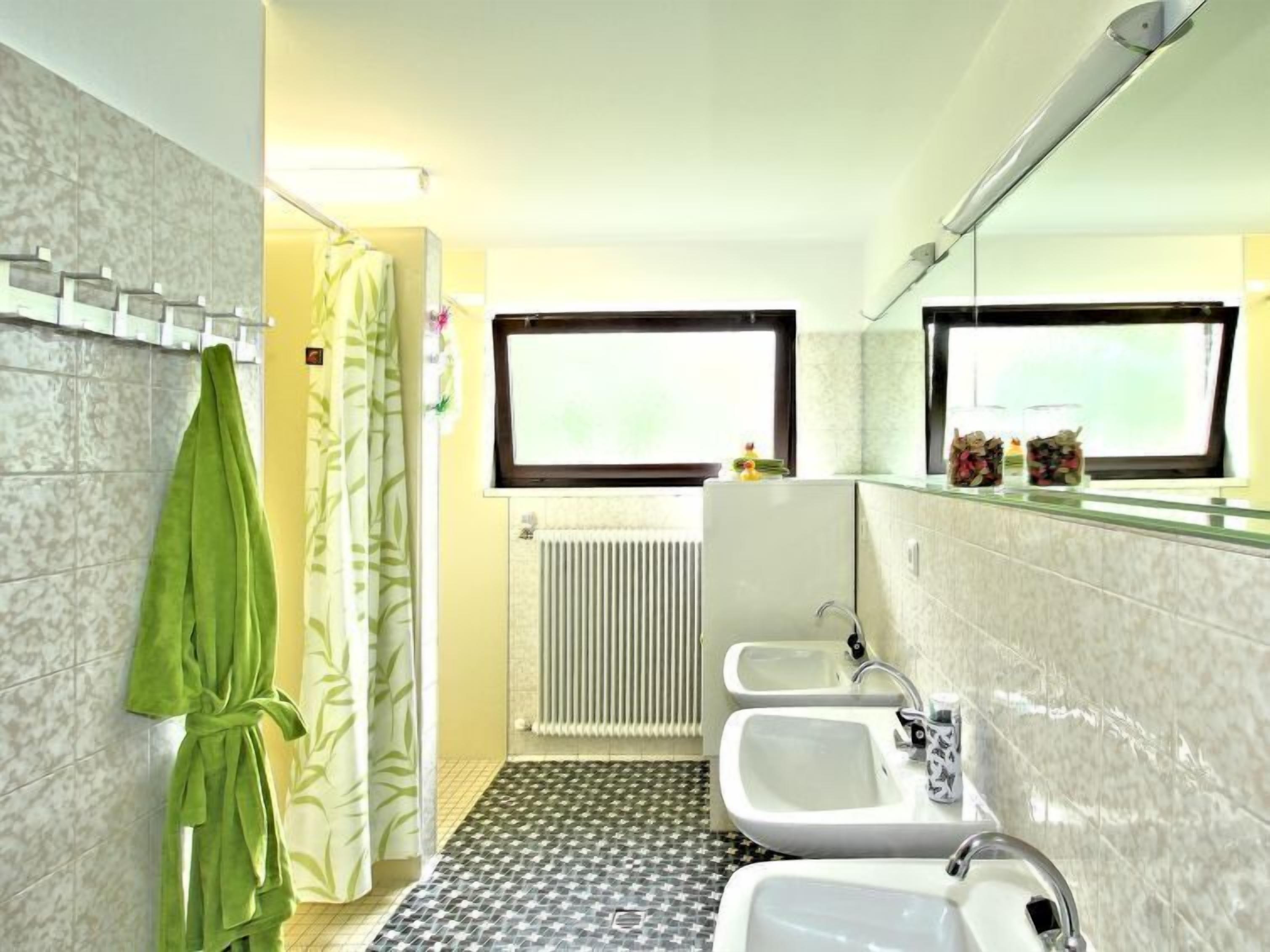 A bathroom with a shower, two sinks, a mirror, and a radiator.