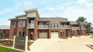 Un immeuble résidentiel moderne à plusieurs étages, doté d’une façade en briques, de nombreux balcons et d’un garage central.