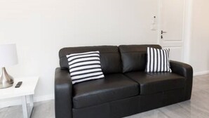 A black leather sofa with two striped pillows, a small white side table with a lamp, and a white door in the background. - Escape to stylish comfort in this modern apartment! (Wagga Wagga)