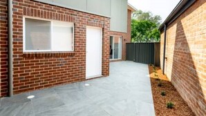 A modern brick house with a garage door, a small window, and a paved driveway. - Escape to stylish comfort in this modern apartment! (Wagga Wagga)