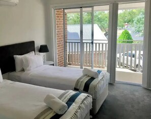 A hotel room with two beds, a balcony with a view of the street, and a brick wall.