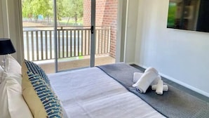 A hotel room with a bed, a TV mounted on the wall, and a sliding glass door leading to an outdoor balcony.