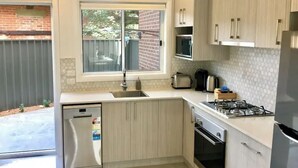 A modern kitchen with light wood cabinets, a stainless steel refrigerator, a built-in oven, and a gas stove.