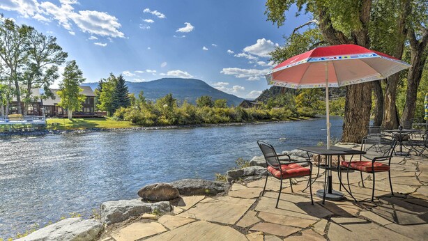 Une terrasse au bord de la rivière, avec un sol en pierre, des sièges d’extérieur et un parasol rouge.