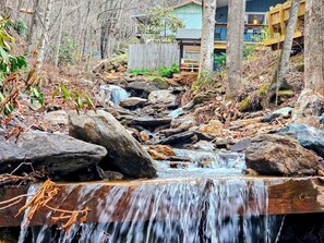 Una cascada en un área boscosa con una terraza de madera y un edificio al fondo.