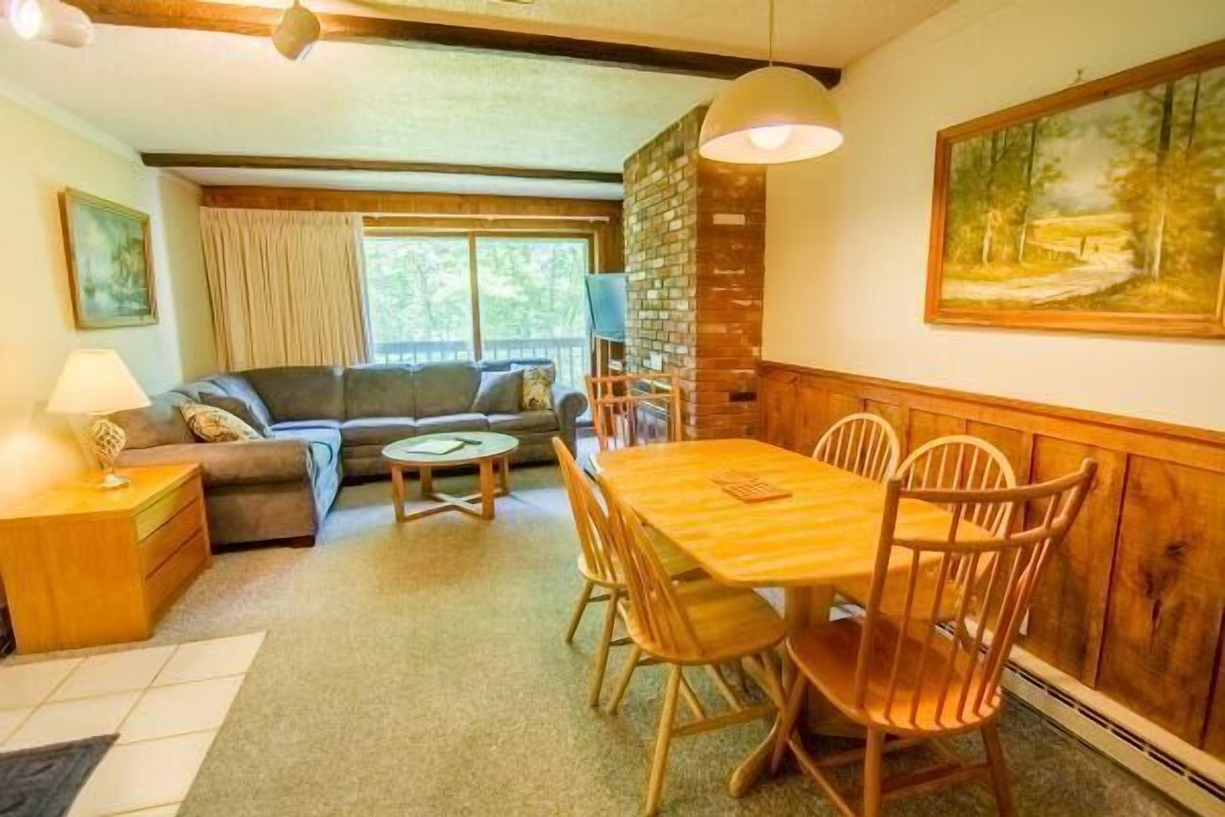 A cozy living room with a sofa, a dining table with chairs, a lamp, and a painting on the wall.