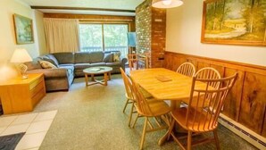 A cozy living room with a sofa, a dining table with chairs, a lamp, and a painting on the wall. - Whiffletree D3 (Killington)