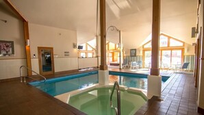 An indoor swimming pool with a separate hot tub area, wooden beams, and a view of the outdoor patio. - Trail Creek 54 (Killington)